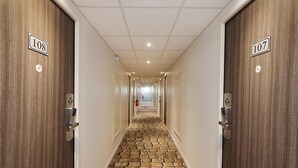 A hotel hallway with a stone-tiled floor, numbered doors, and a ceiling with recessed lighting. - B&B Hôtel Albi (Albi)
