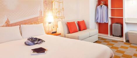 A hotel room with a large bed, a nightstand, a sofa, a wardrobe, and a suitcase.