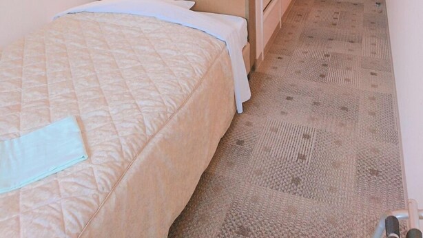 A hotel room with a bed, bedside table, lamp, and a door leading to another room. - Good Inn Kagoshima (Kagoshima)