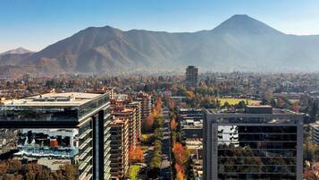 A cityscape with modern buildings, a mountain in the background, and autumn-colored trees.