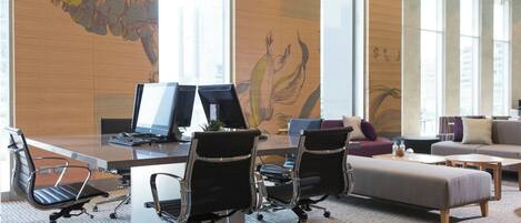 A modern office space with a large desk, two computer monitors, office chairs, a sofa, and a patterned carpet.