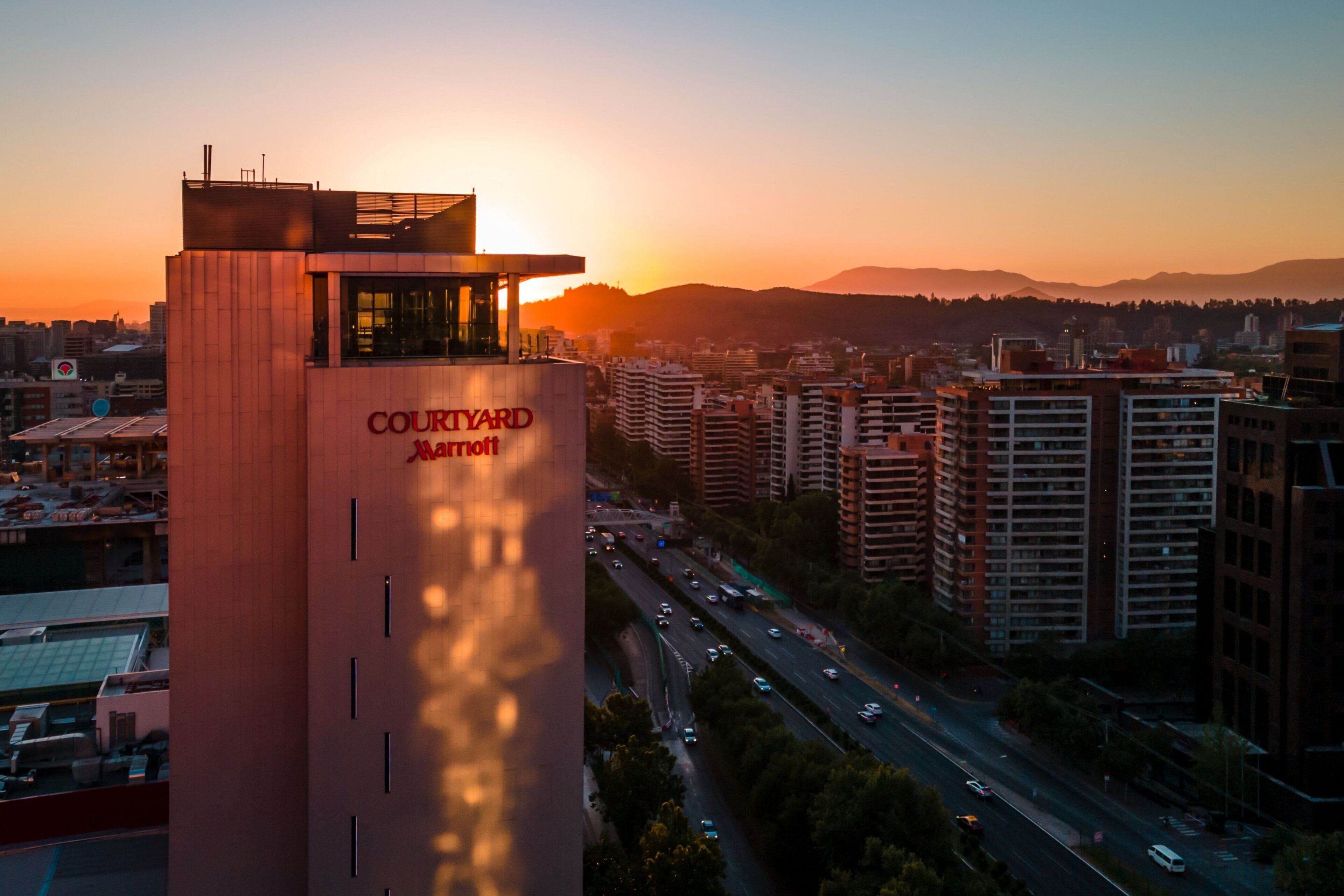 A Courtyard by Marriott hotel with a view of the sunset over a cityscape.