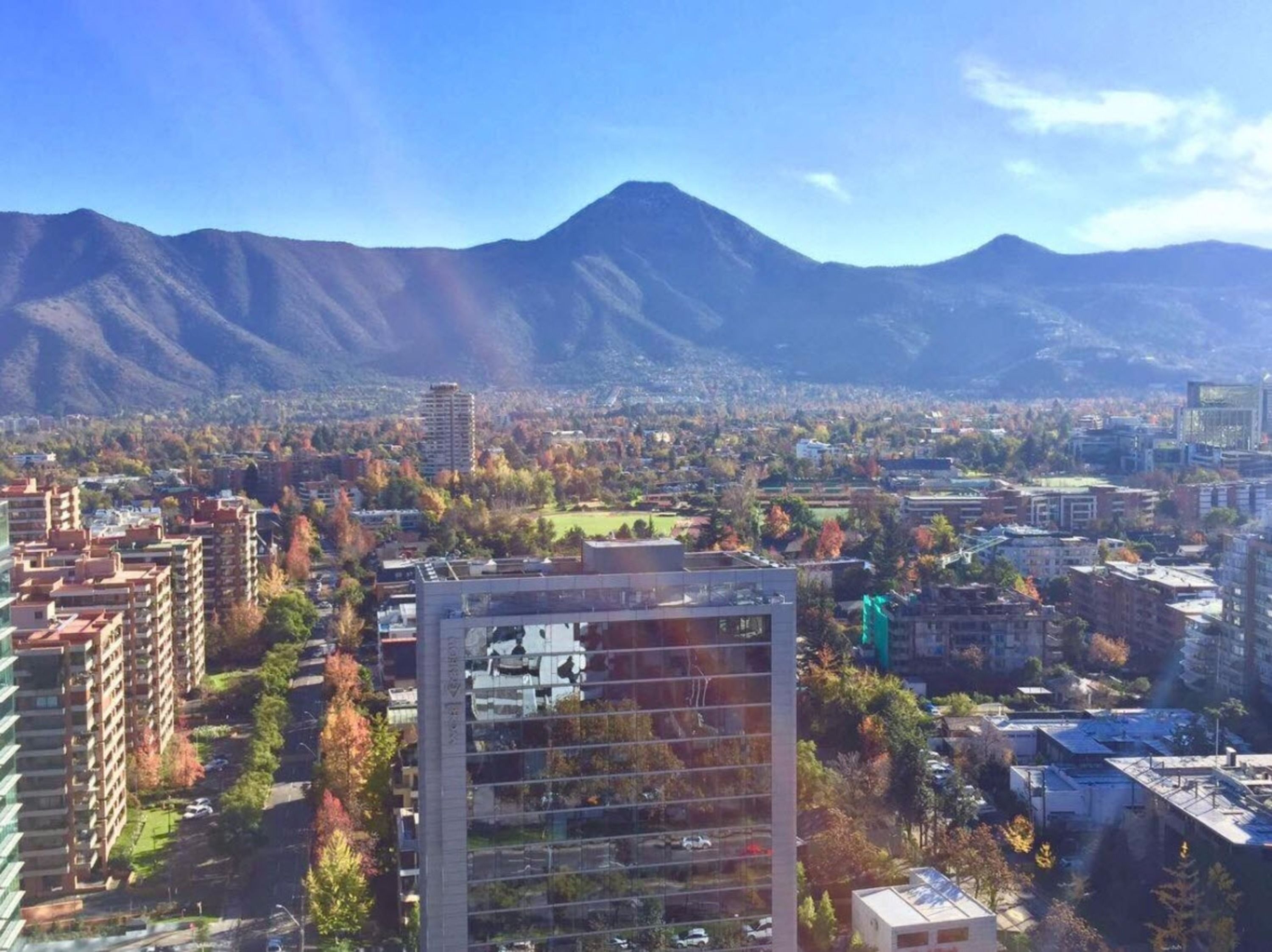 Un paysage urbain avec une montagne imposante en arrière-plan, des bâtiments modernes et un mélange de constructions résidentielles et commerciales.