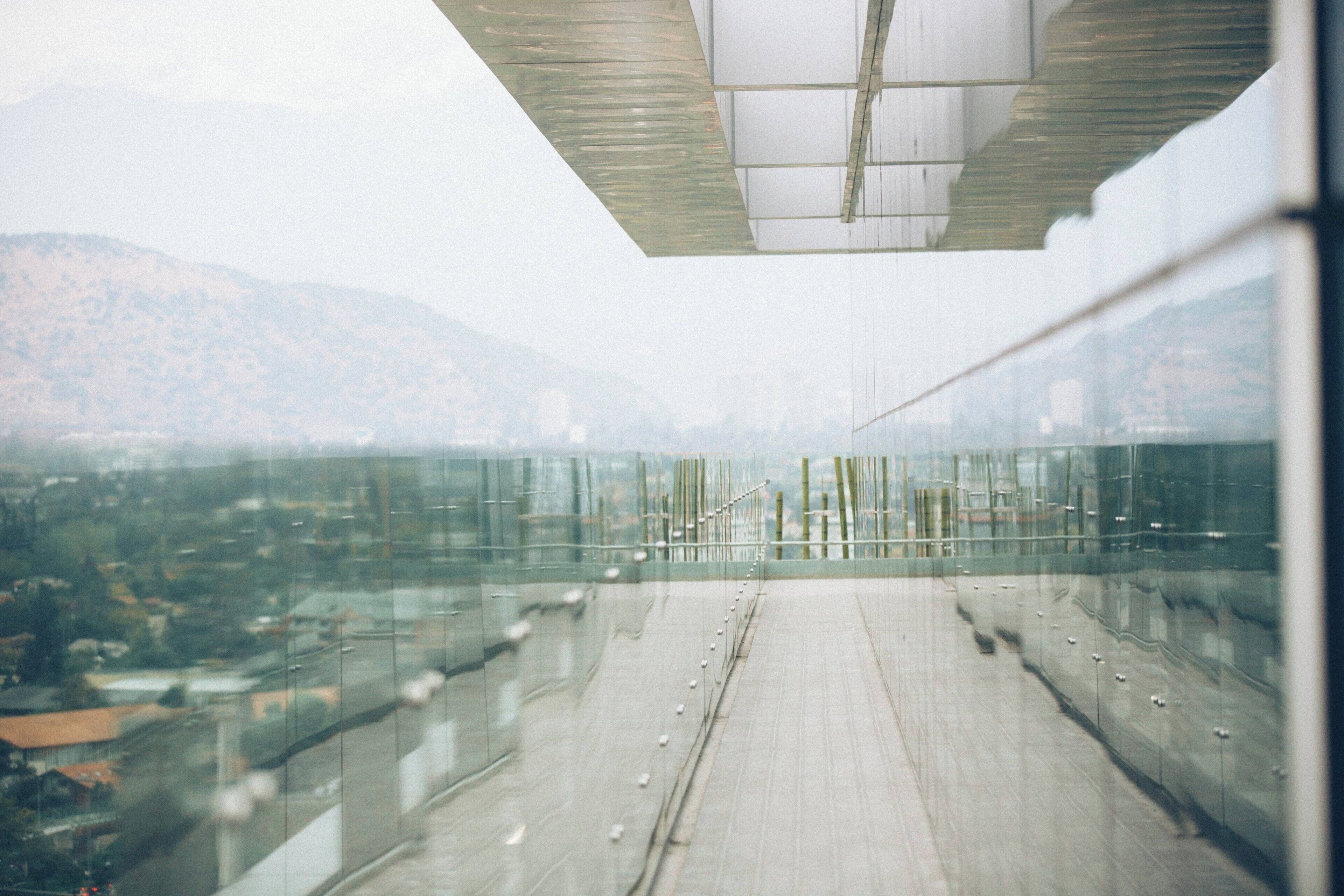 A modern building with a glass facade, a concrete floor, and a view of a cityscape and mountains in the background.