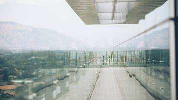 A modern building with a glass facade, a concrete floor, and a view of a cityscape and mountains in the background.