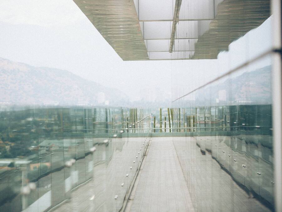 A modern building with a glass facade, a concrete floor, and a view of a cityscape and mountains in the background.