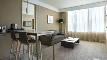 A modern hotel room with a dining area, sofa, and a large window with curtains.