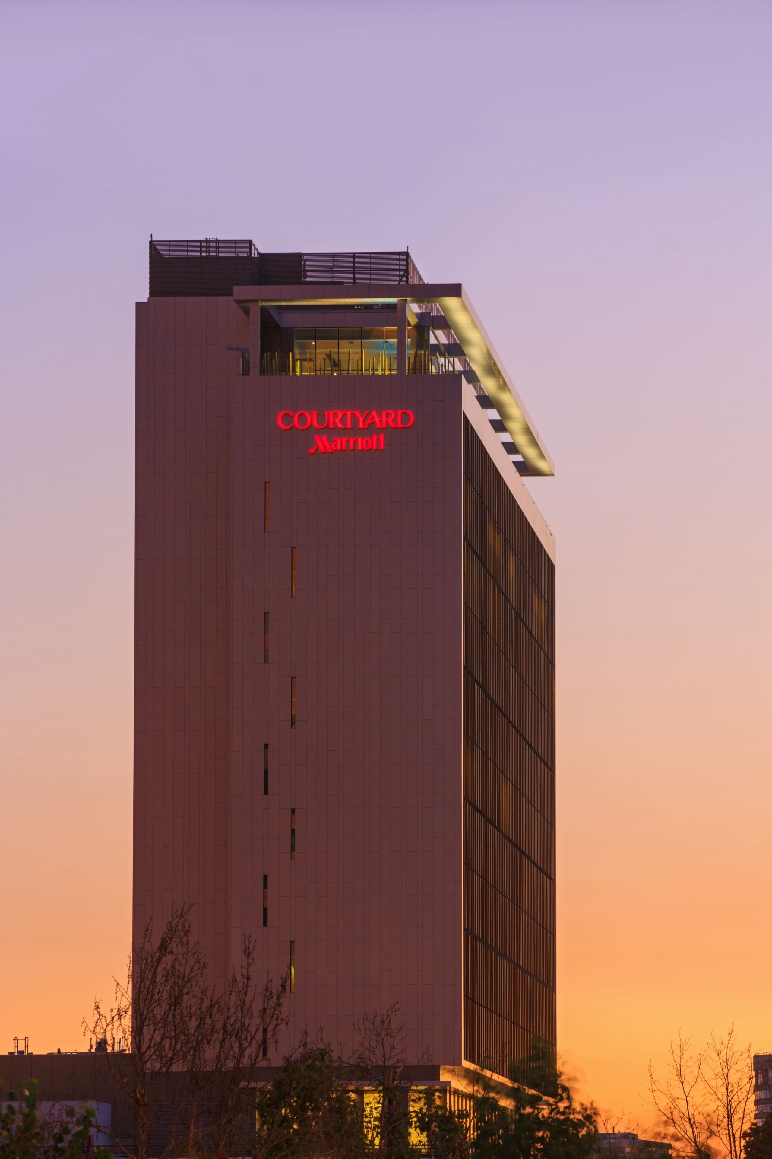 A Courtyard Marriott hotel with a modern design, featuring a prominent vertical stripe pattern and a rooftop terrace.