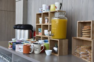 Ein Frühstücksbuffet mit verschiedenen Tassen, einem großen Glasgefäß mit Orangensaft und Kuchengitter.