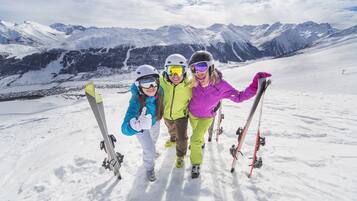 Tres personas en una montaña nevada con esquíes, de pie en una zona llana con un telesilla al fondo.
