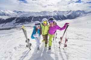 Tres personas en una montaña nevada con esquíes, de pie en una zona llana con un telesilla al fondo.
