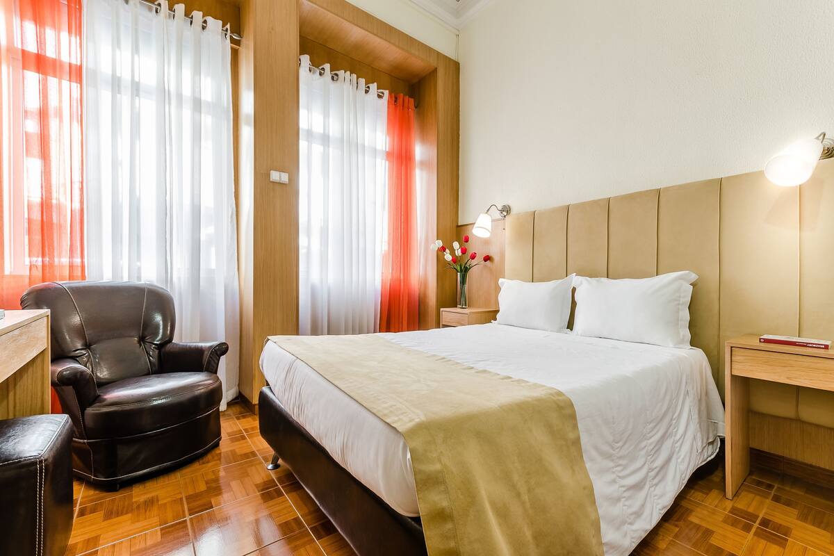 Een hotelkamer met een bed, een stoel, een nachtkastje en een lamp.