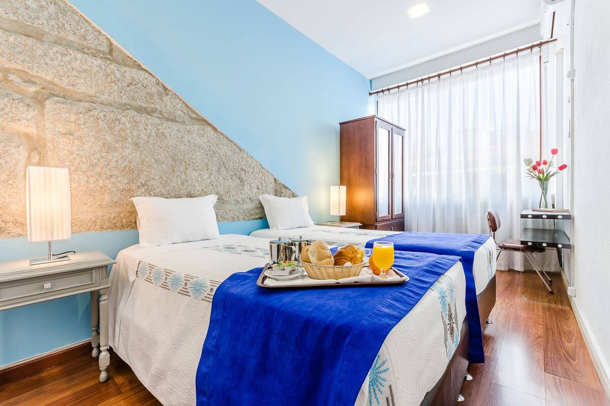 Een hotelkamer met twee bedden, een accentmuur van steen, een houten kast en een ontbijttafel op de bedden.