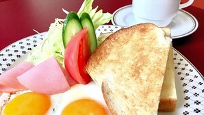 Ein Teller mit Toast, Eiern, Schinken und Gemüse, dazu eine Tasse Kaffee auf einem Tisch.