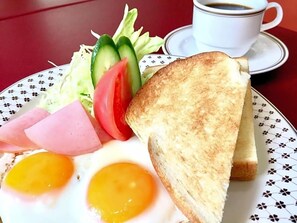 Ein Teller mit Toast, Eiern, Schinken und Gemüse, dazu eine Tasse Kaffee auf einem Tisch.