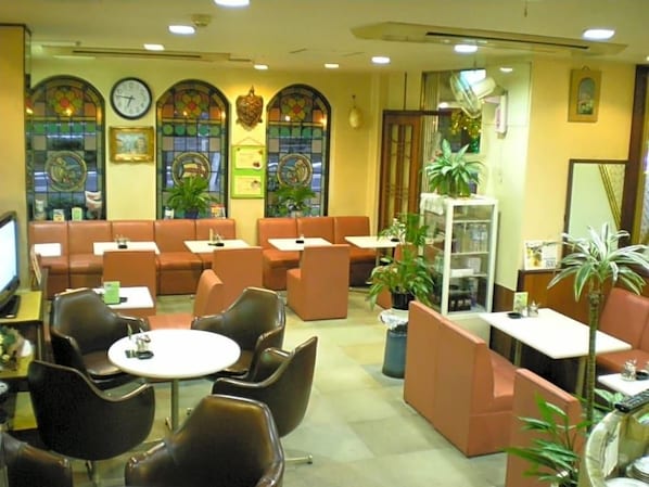 Un restaurant amb seients a caixa i taules, un rellotge a la paret i plantes en testos.