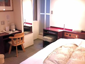Ein Hotelzimmer mit einem Bett, einem Schreibtisch, einem Sessel, einem kleinen Tisch und einem Fenster.