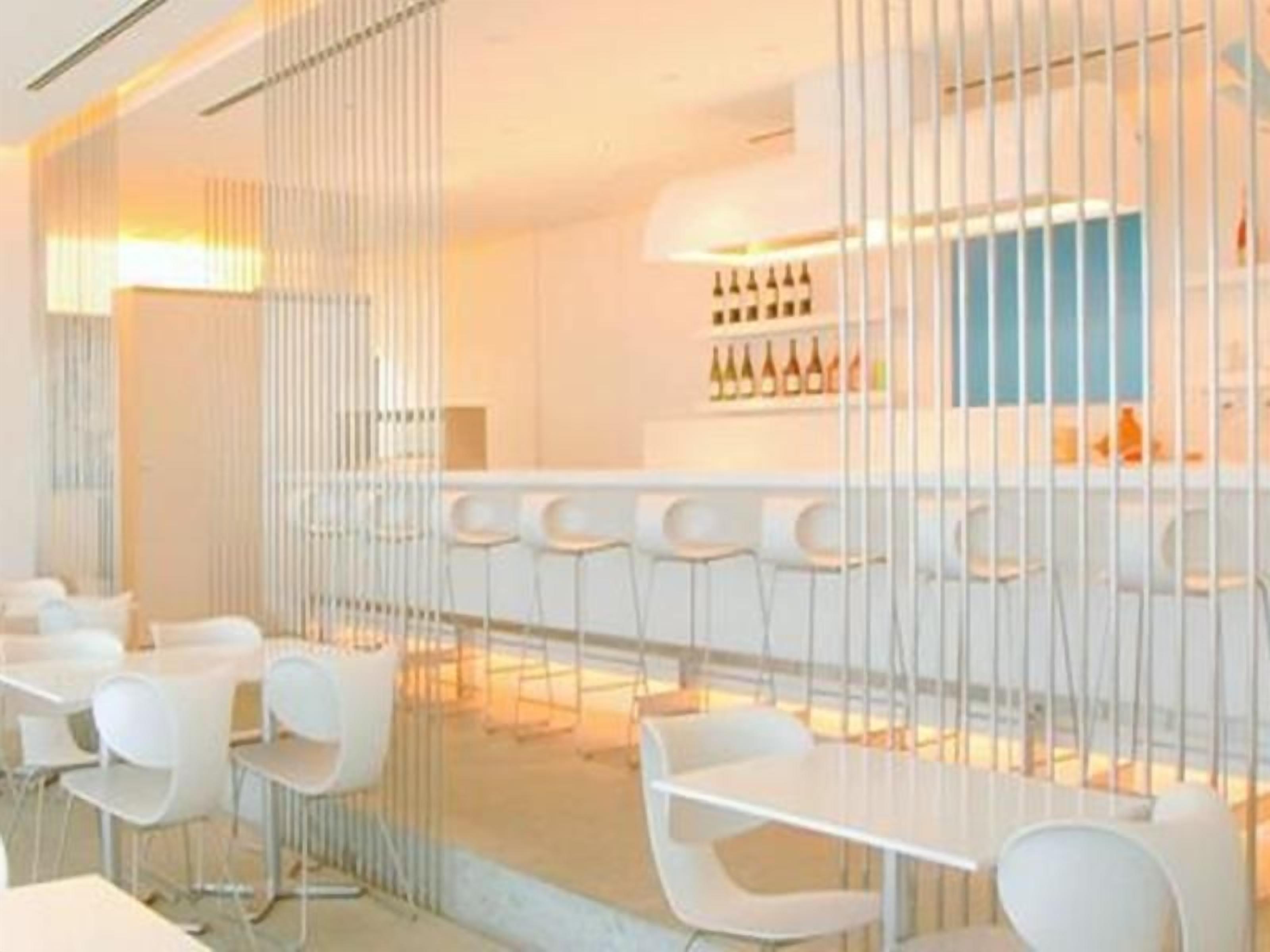 Zona de bar moderna con taburetes blancos y una vitrina de vinos.