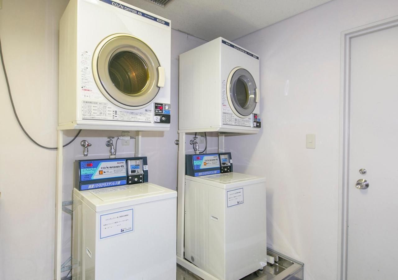Two stacked washing machines with control panels, a white door, and a metal shelf.