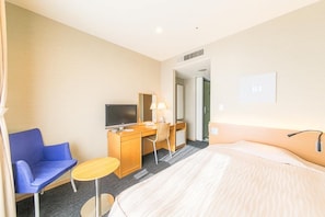 Una habitación de hotel con una cama, un escritorio, una silla, un televisor y una mesita.