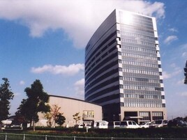 Un moderno edificio de gran altura con fachada de vidrio, rodeado de coches estacionados y vegetación.