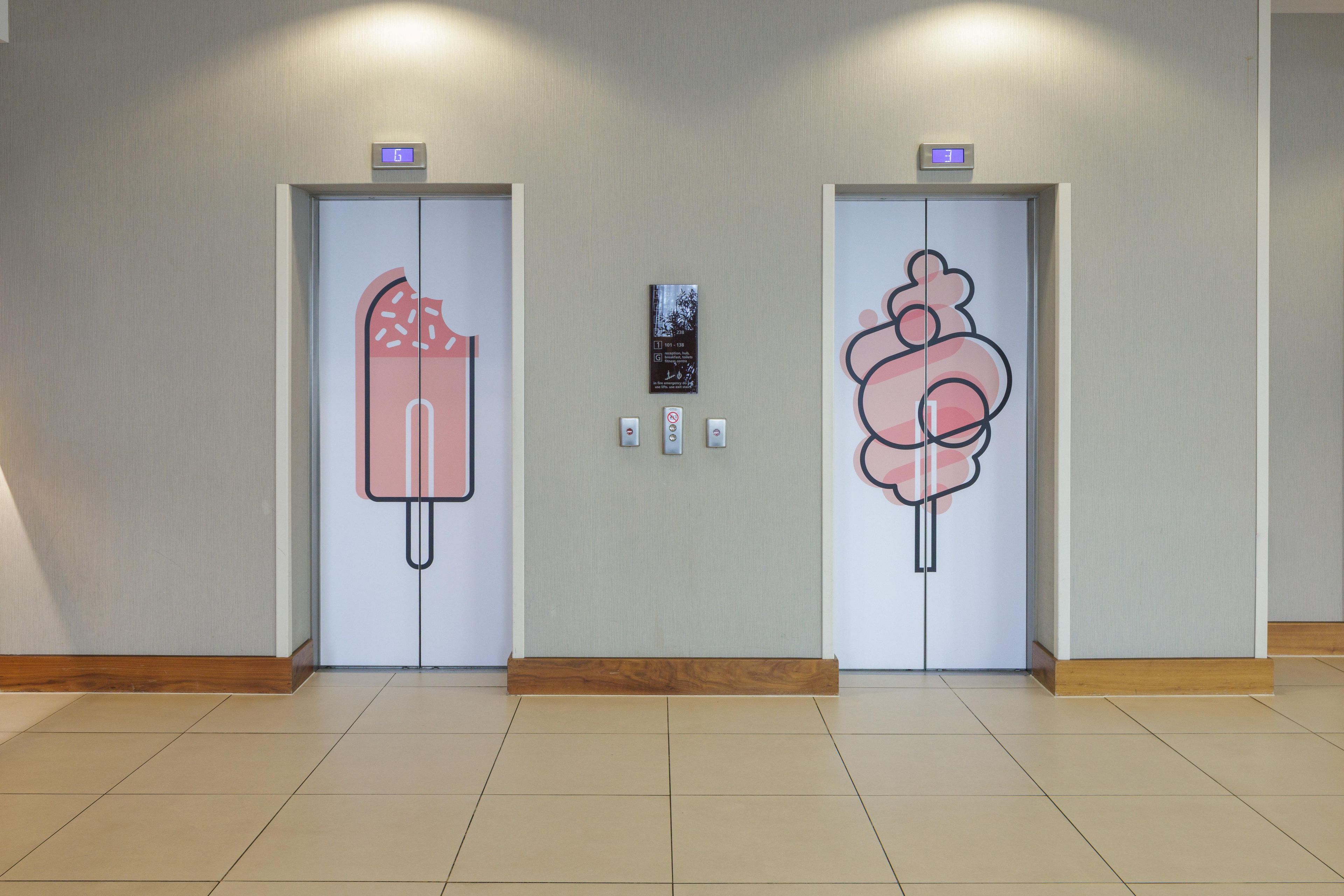 Two elevator doors with a frosty design, a fire alarm, and a digital display above each door.