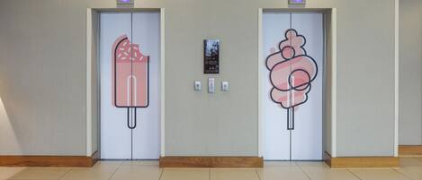 Two elevator doors with a frosty design, a fire alarm, and a digital display above each door.
