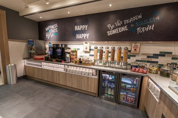 Una estación autoservicio para bebidas con dispensadores, opciones de bebidas frías y una variedad de bocadillos.