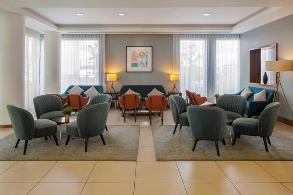 A modern hotel lobby with a central seating area, a large window with curtains, and a framed artwork on the wall. - Hampton by Hilton Bournemouth (Bournemouth)