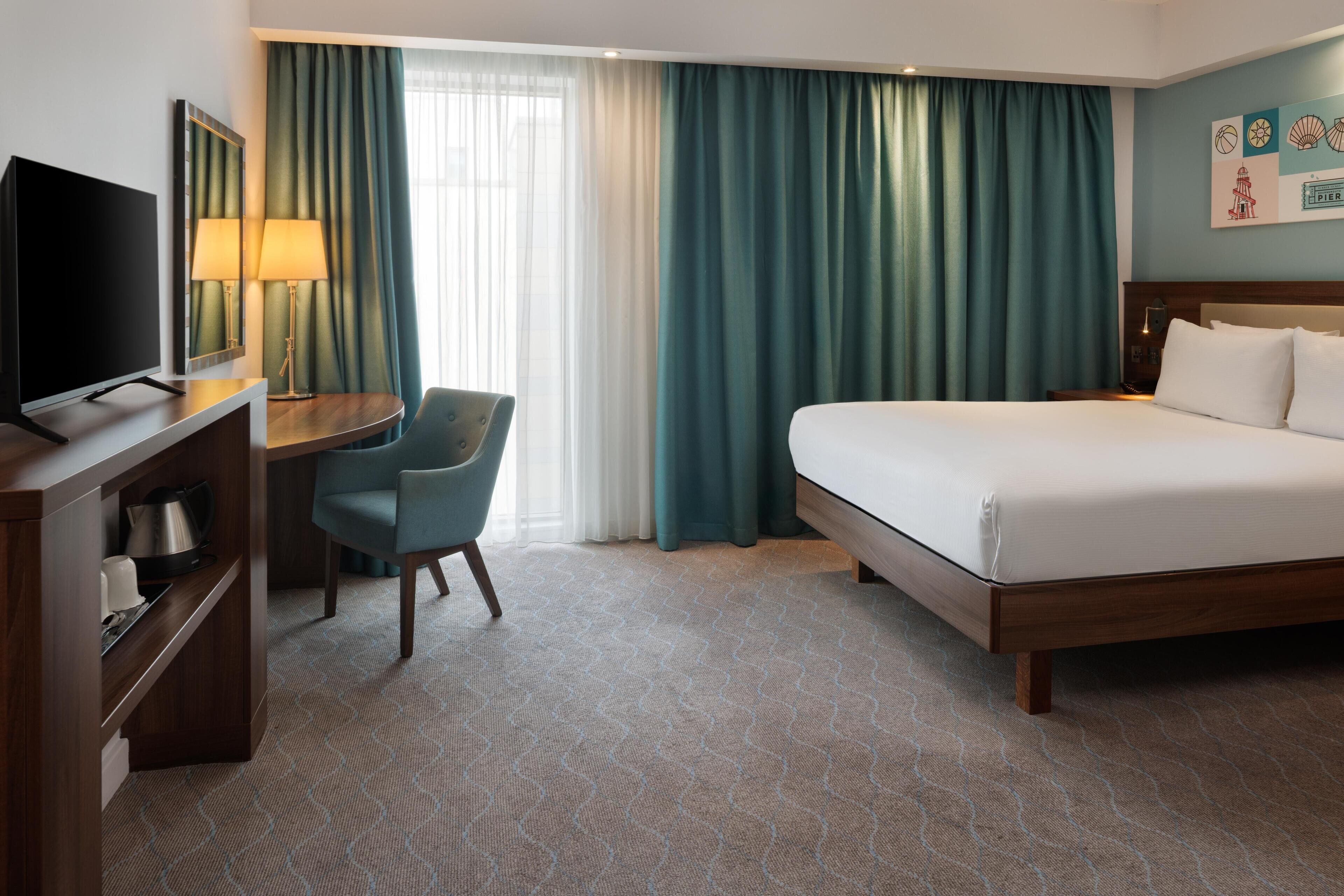 Una habitación de hotel con una cama, un escritorio con lámpara, un televisor y una silla.