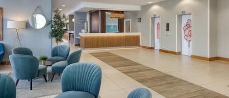 Un hall de hotel con una recepción, zona de estar y una planta grande.