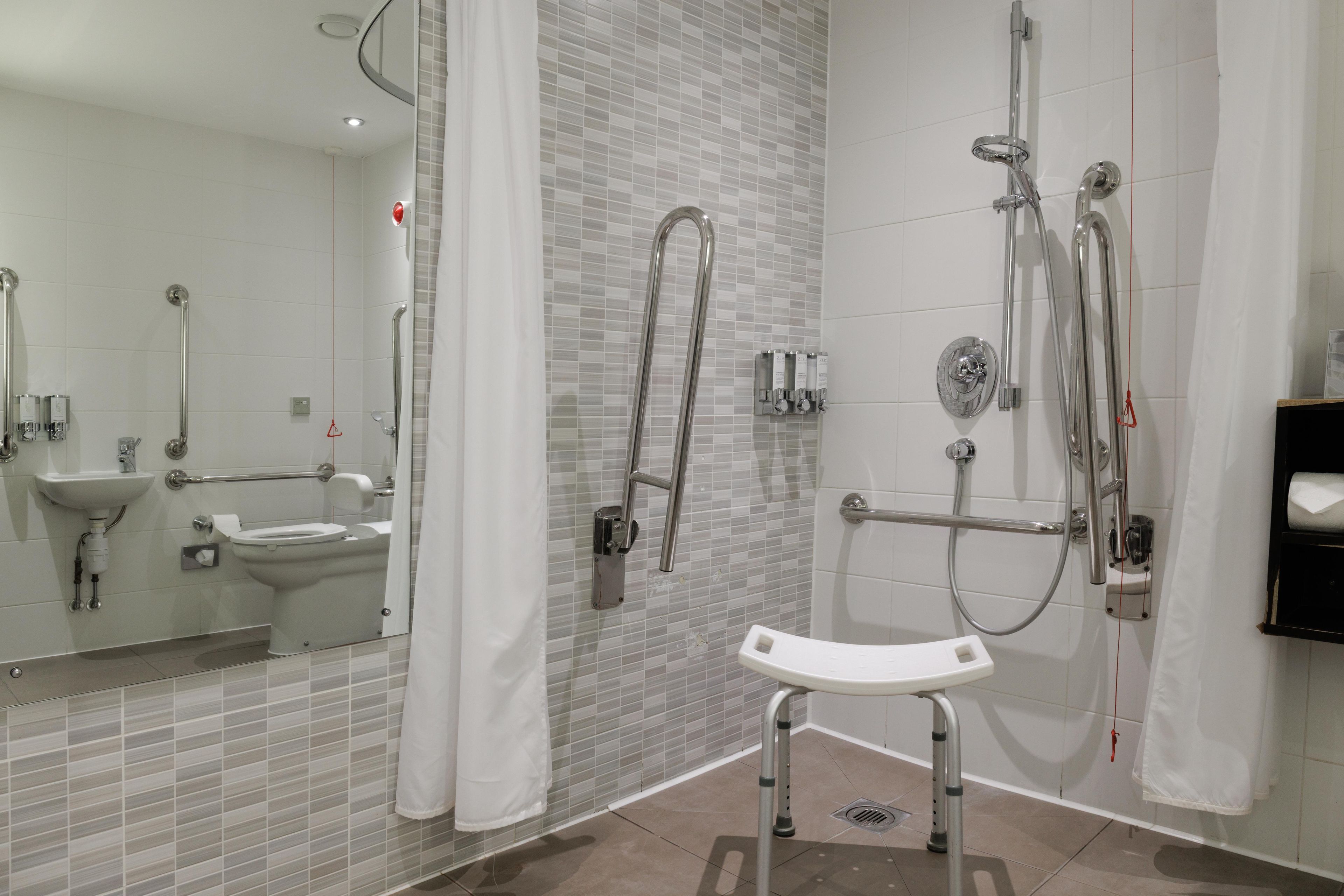 A modern bathroom with a walk-in shower, grab bars, a toilet with a safety seat, and a sink.