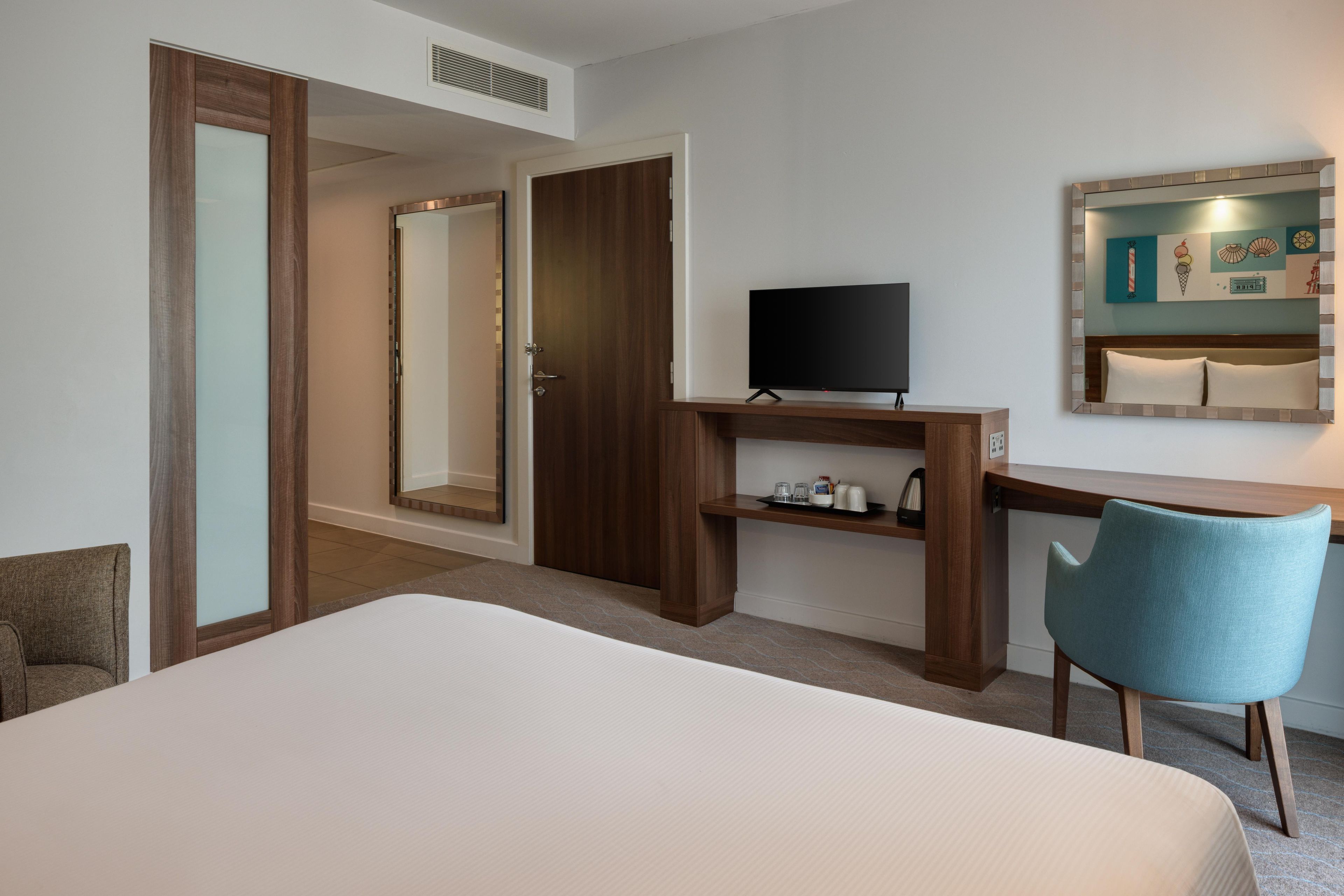 Una camera d'albergo con un letto, una scrivania con televisore, una sedia e uno specchio.
