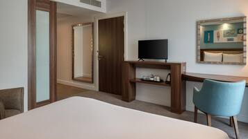 A hotel room with a bed, a desk with a television, a chair, and a mirror.