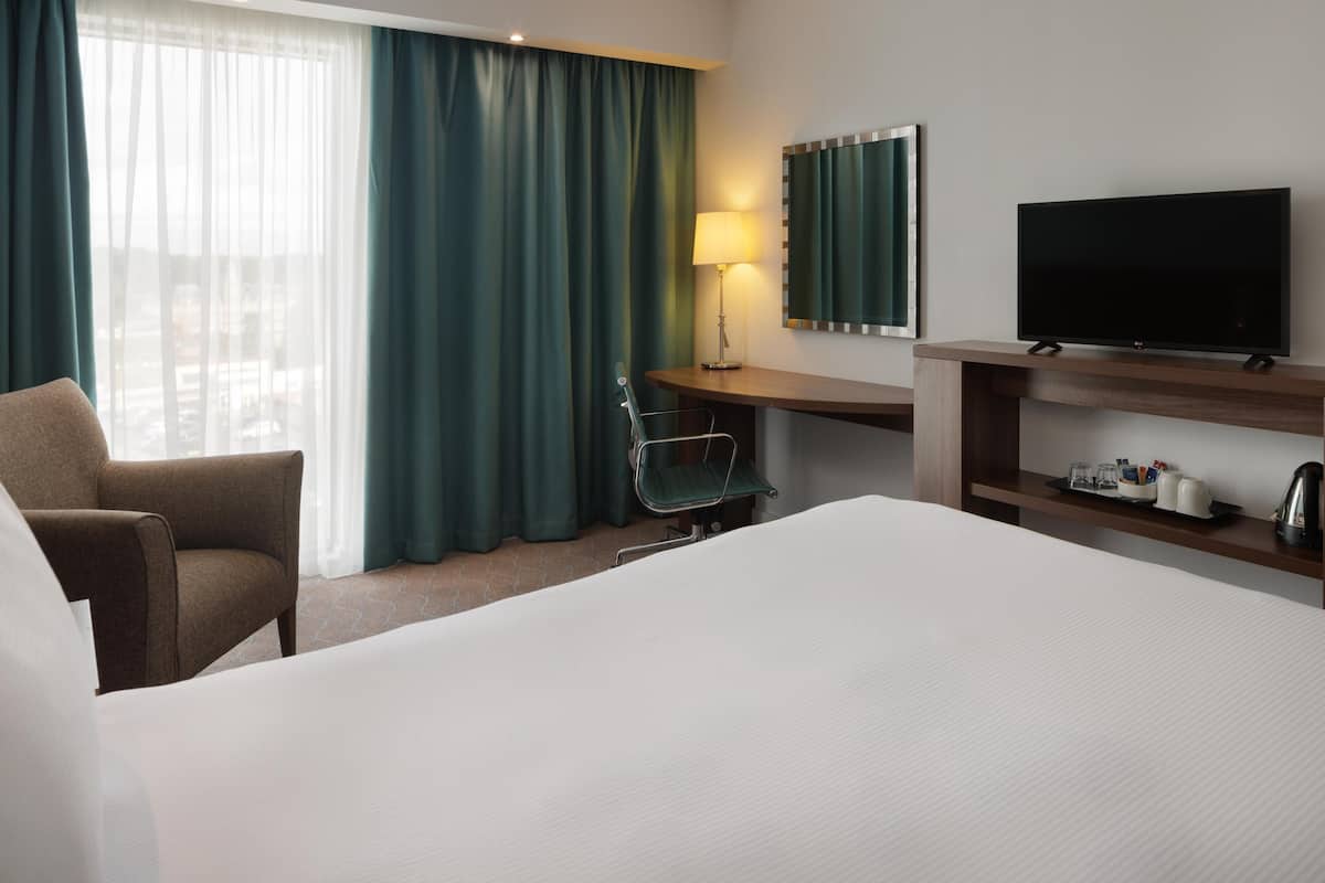 A hotel room with a bed, a desk, a chair, a TV, and a window with curtains.