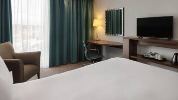 Habitación de hotel con cama, escritorio, silla, televisor y ventana con cortinas.