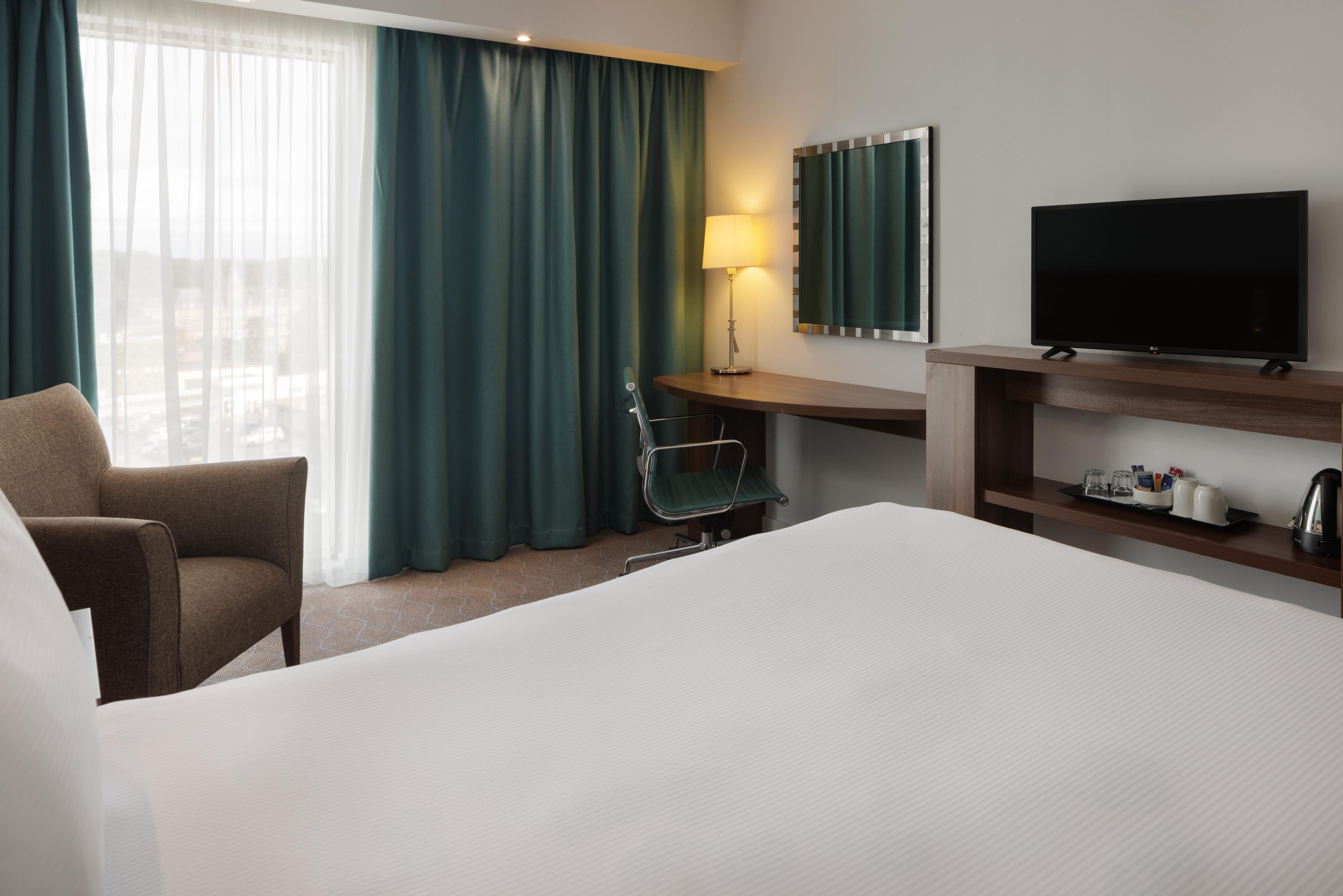 A hotel room with a bed, a desk, a chair, a television, and a window with curtains.