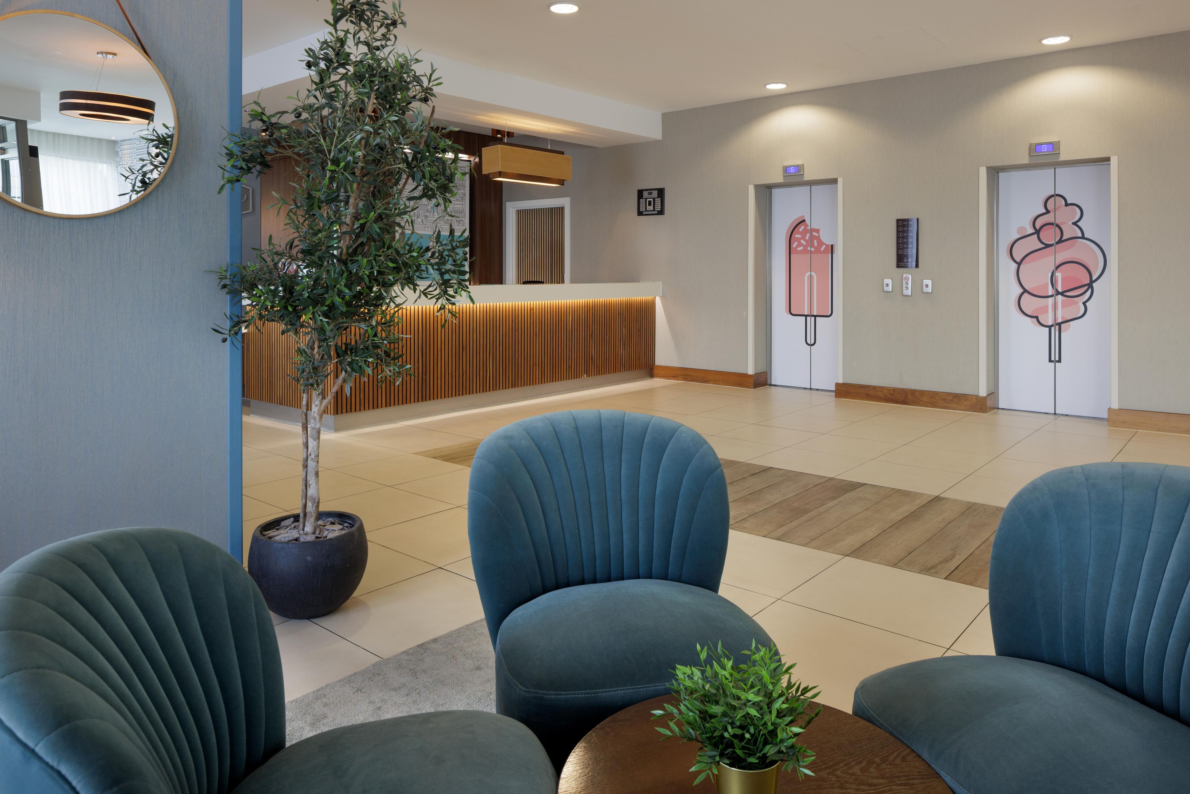 A reception area with a potted plant, blue upholstered chairs, a wooden reception desk, and a wall-mounted clock.