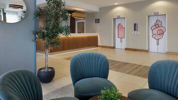 A reception area with a potted plant, blue upholstered chairs, a wooden reception desk, and a wall-mounted clock.