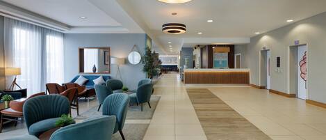 Un hall de hotel con zonas de estar, un mostrador de recepción y un espejo grande.