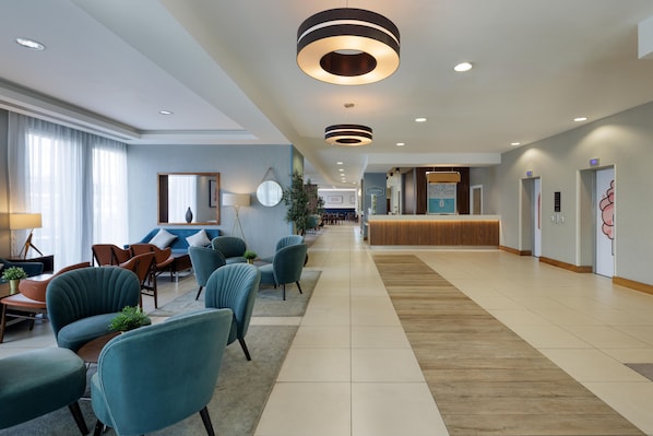 Un hall de hotel con zonas de estar, un mostrador de recepción y un espejo grande.