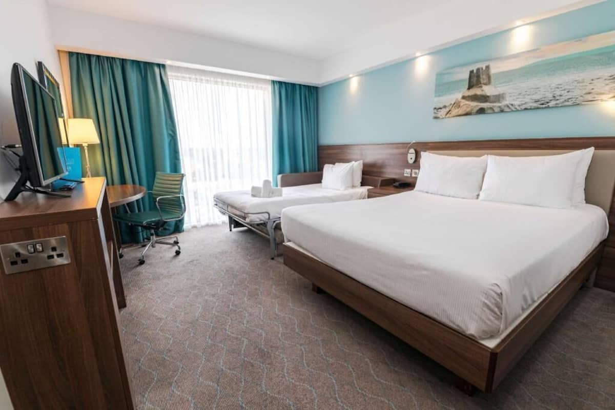 A hotel room with two beds, a desk with a computer, a chair, and a window with curtains.