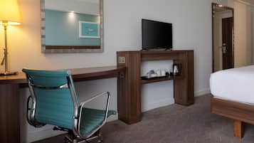 A hotel room with a desk, a chair, a bed, a television, and a mirror.