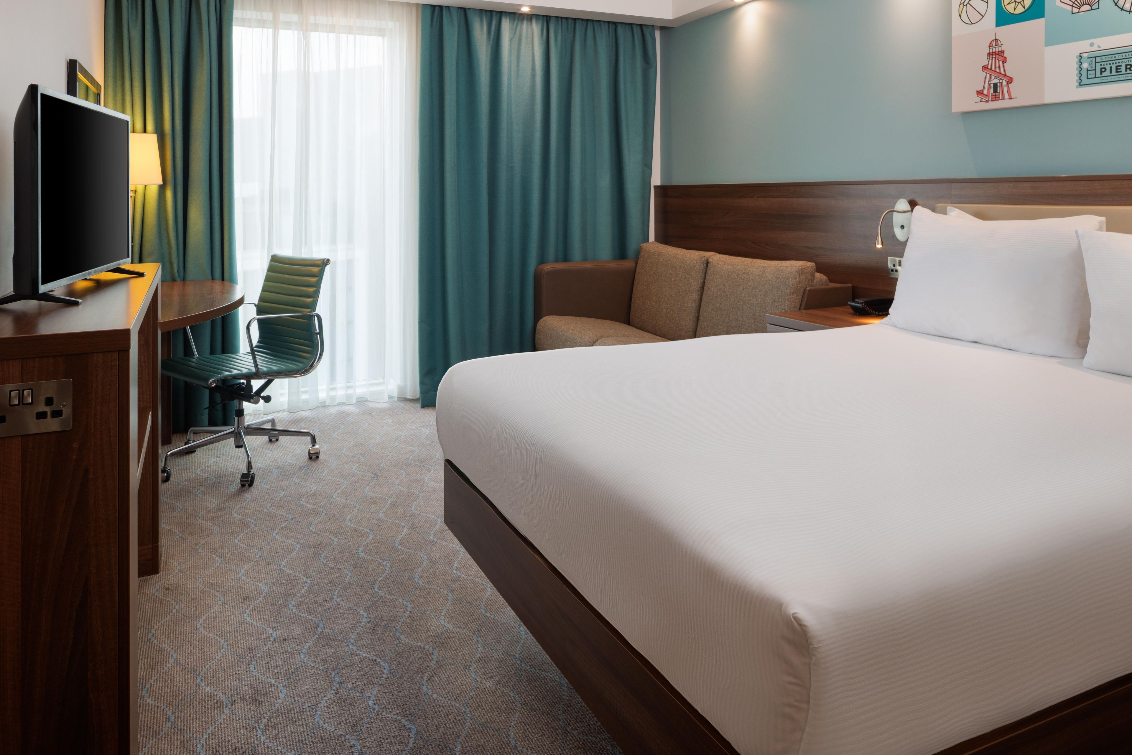 Una habitación de hotel con cama, escritorio con televisor, silla y sofá.