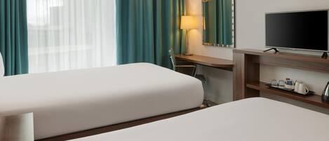 A hotel room with two beds, a desk, a television, a lamp, and a mirror.