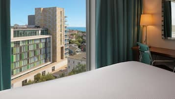 A hotel room with a bed, a desk, and a view of a cityscape.