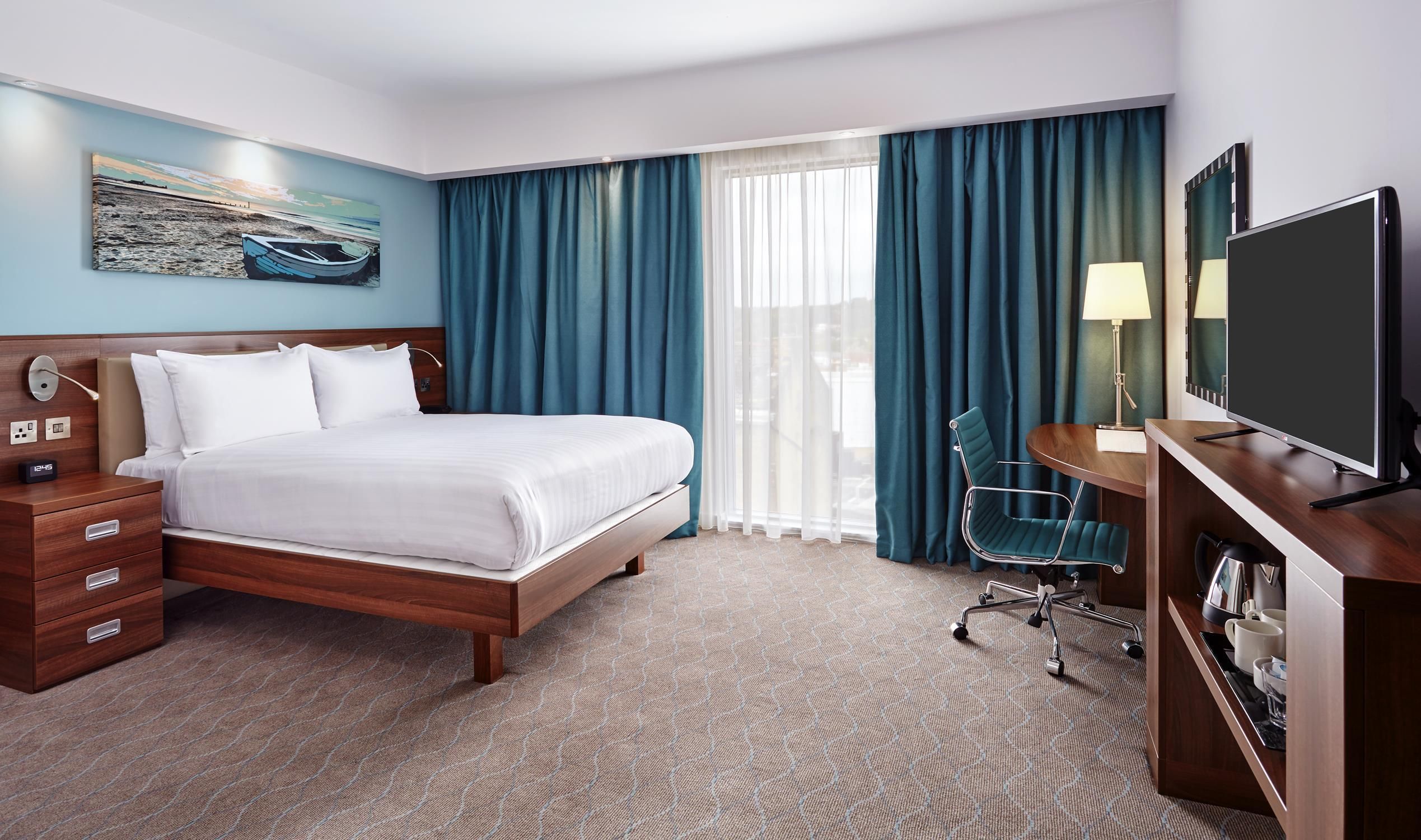 A hotel room with a bed, a desk, a TV, and a window with curtains.