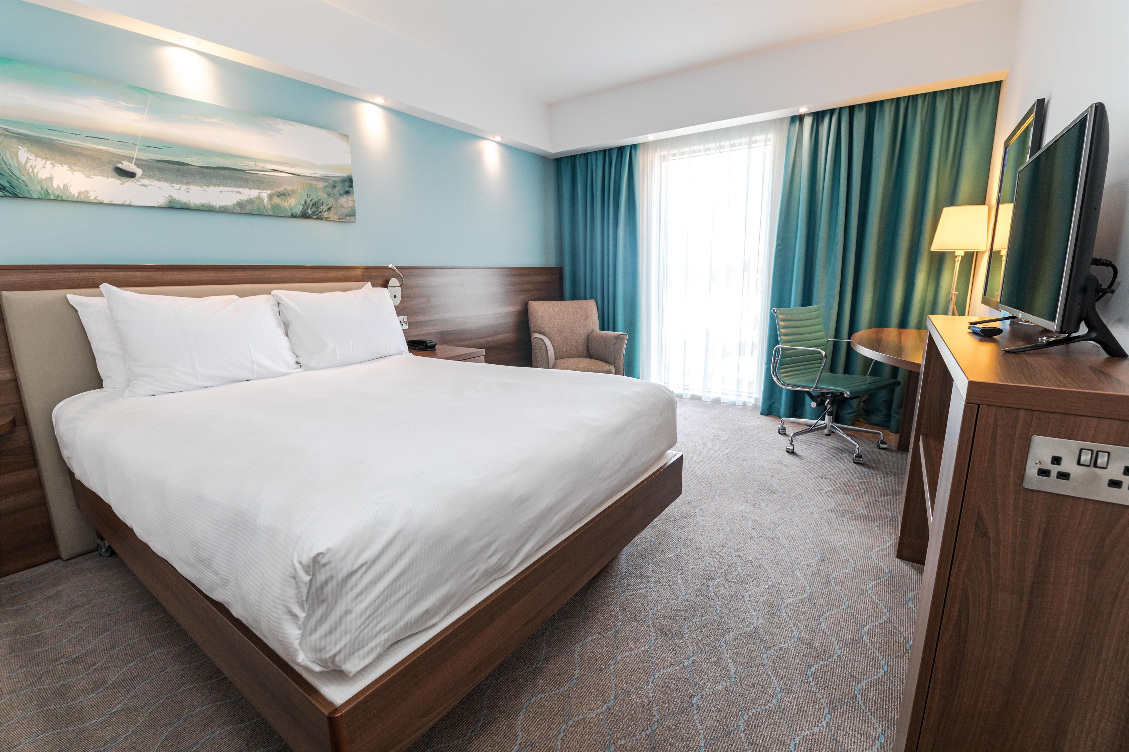 Een hotelkamer met een groot bed, een bureau met een computer, een stoel en een raam met gordijnen.