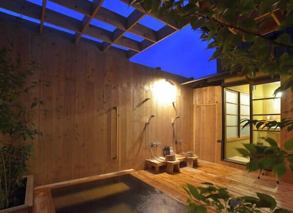Un spa de madera con hidromasaje, paredes de madera y una puerta de cristal que da a una habitación tradicional.