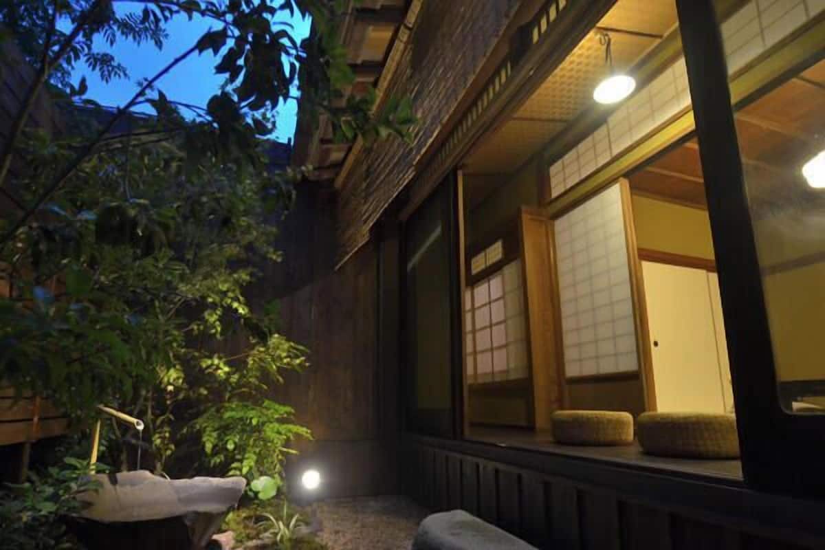 A traditional Japanese-style building with a wooden exterior, a stone pathway, and a small garden with a stone lantern and plants.
